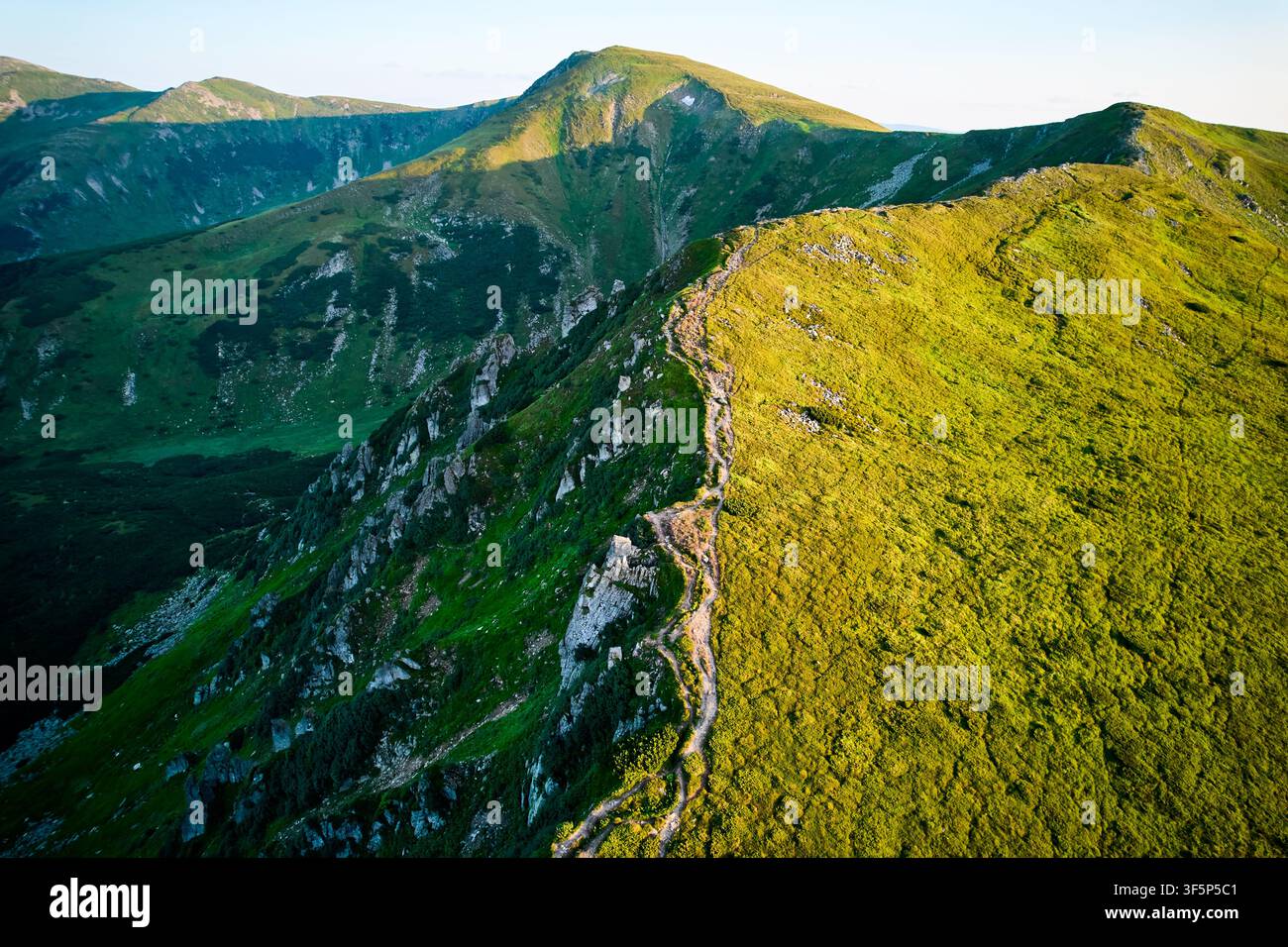 Vue aérienne de la chaîne de montagnes accidentée avec des pentes verdoyantes au coucher du soleil. Paysage met en valeur la beauté de la nature intacte avec des sommets lointains et des vallées baignées de lumière douce du soleil. Carpates, Chornogora. Banque D'Images