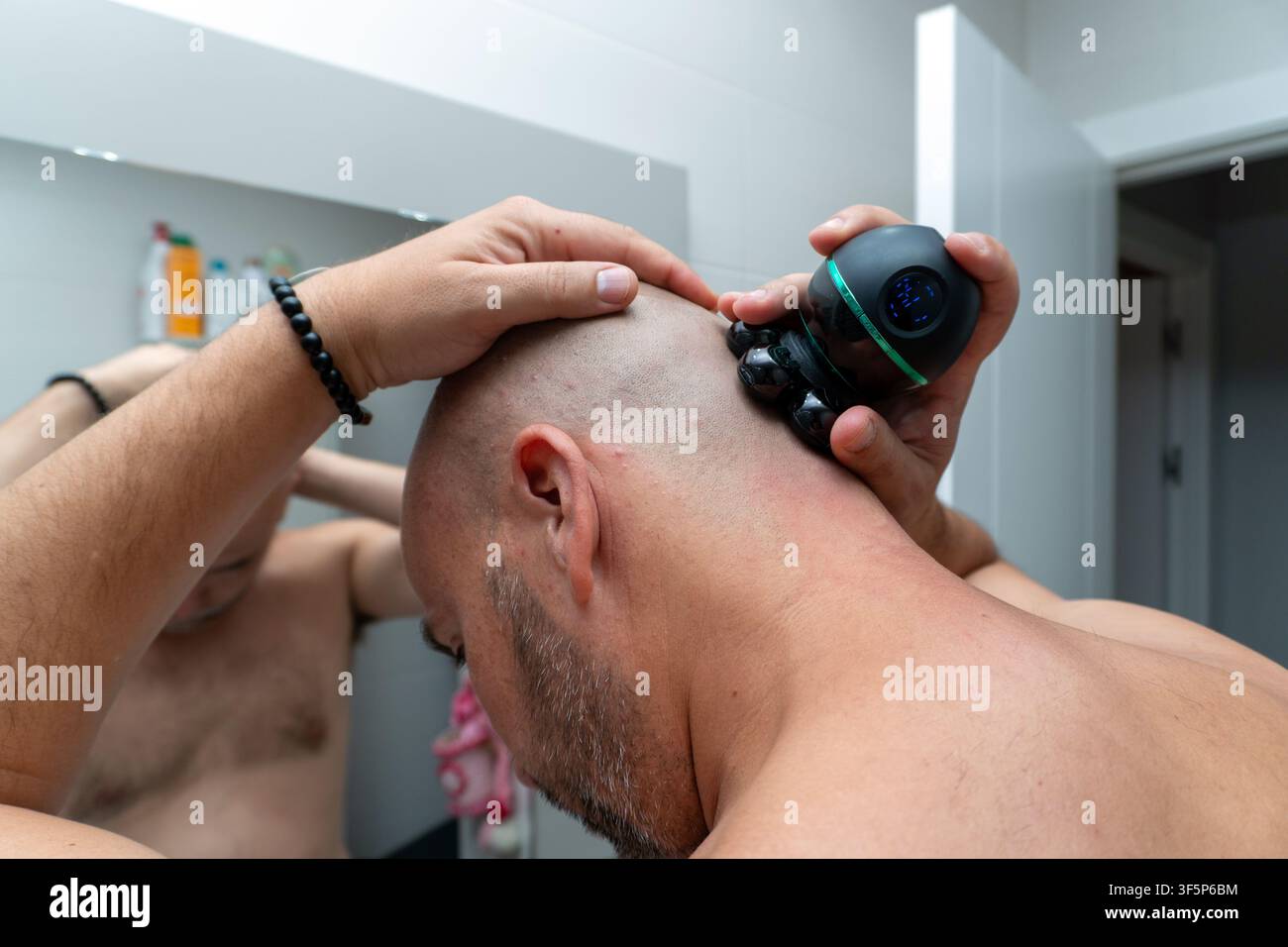 Homme se rasant la tête avec un rasoir électrique dans la salle de bain Banque D'Images