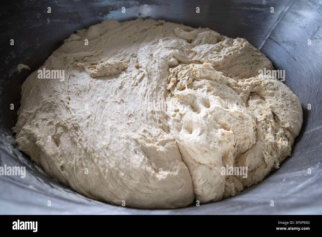 Une pâte blanche fraîche se trouve dans un grand bol industriel métallique pour le proofing dans un cadre de cuisine professionnelle alors que le mélange de farine brute subit la préparation Banque D'Images
