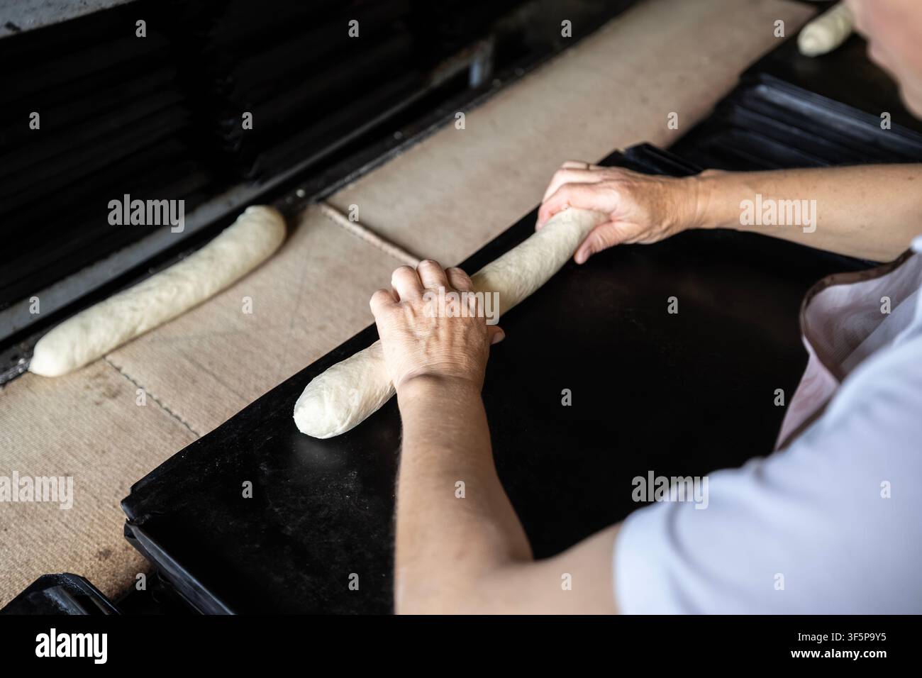Le boulanger modèle la pâte crue sur un plateau métallique pour la production de pain artisanal dans un atelier commercial avec un équipement de chaîne de montage en arrière-plan capturant p Banque D'Images