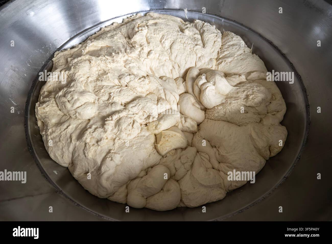 Pâte brute fraîche dans un grand bol mélangeur industriel en métal brillant, préparée pour la cuisson de délicieux produits de boulangerie dans une boulangerie professionnelle Banque D'Images