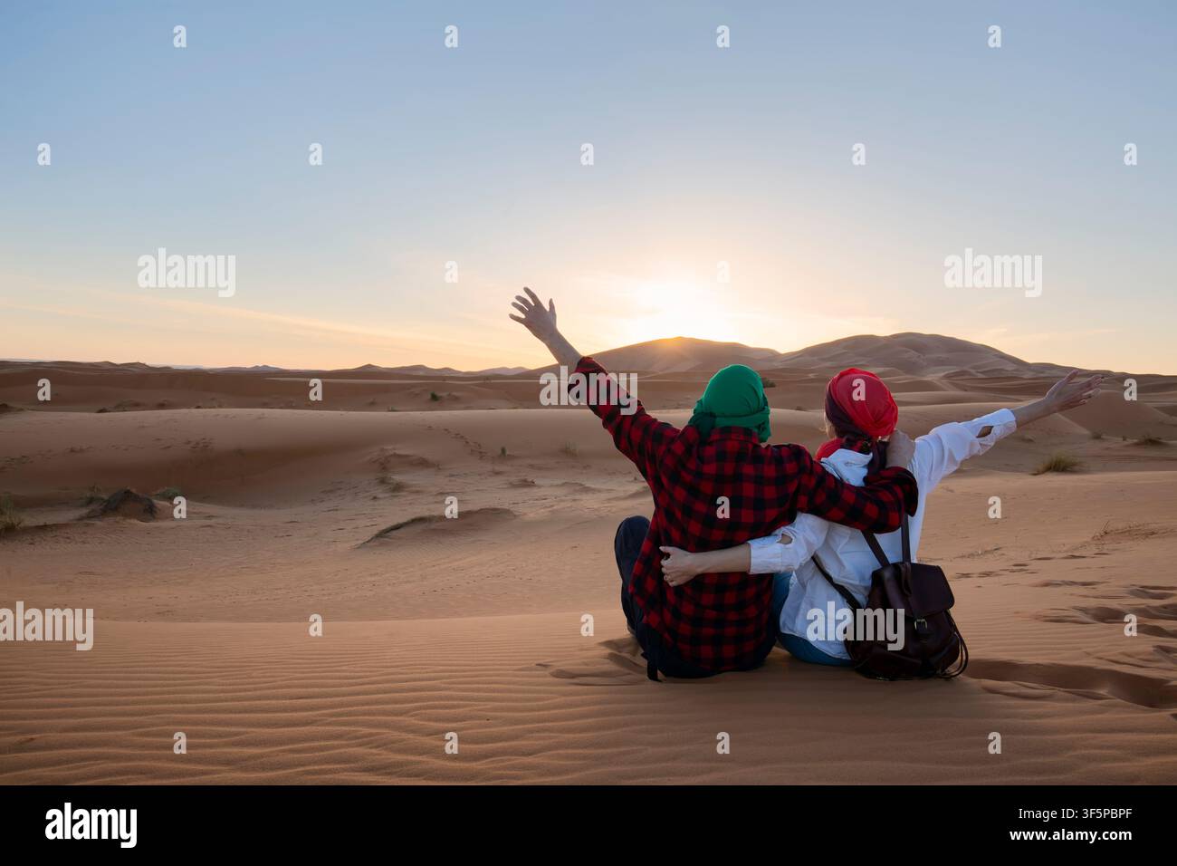 Couple amoureux assis les bras levés dans le désert du Sahara. Maroc. Banque D'Images