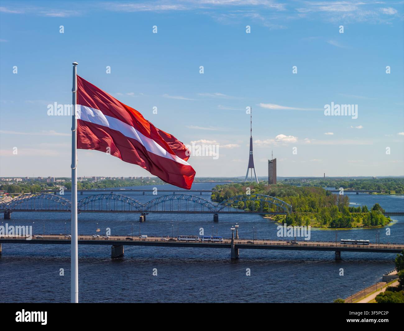 Drapeau letton avec la tour de télévision de Riga et le pont ferroviaire par une journée d'été ensoleillée Banque D'Images
