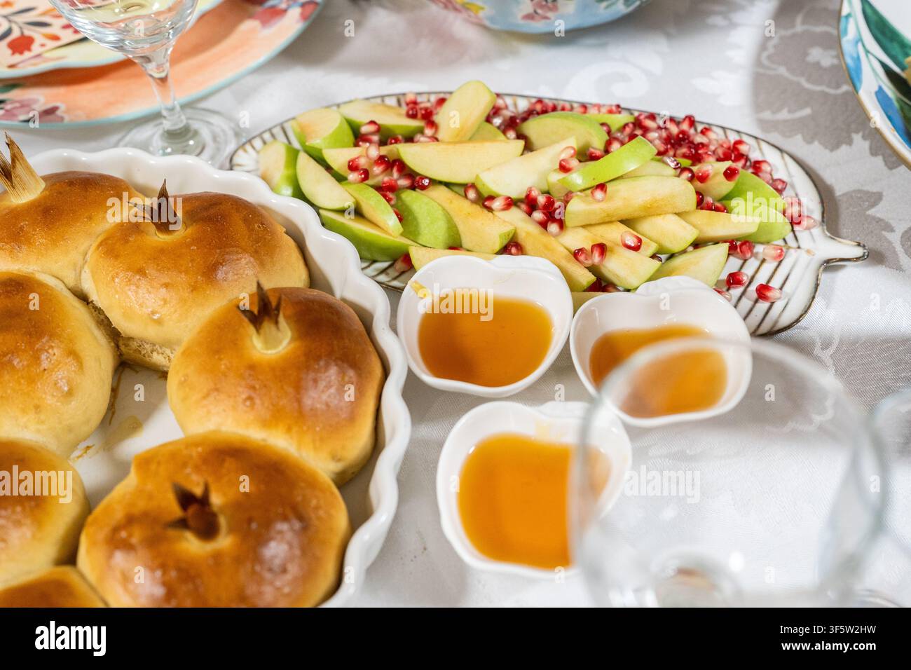 Une mise en table festive montre un pain challah rond et des pommes tranchées avec du miel à côté. Il y a des graines de grenade sur les pommes. Cela fait partie des traditions de Rosh Hashanah. Banque D'Images