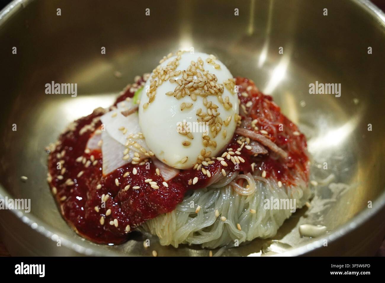 Nouilles de sarrasin froides épicées Bibim-Naengmyeon avec sauce rouge et œuf dans un bol en laiton Banque D'Images