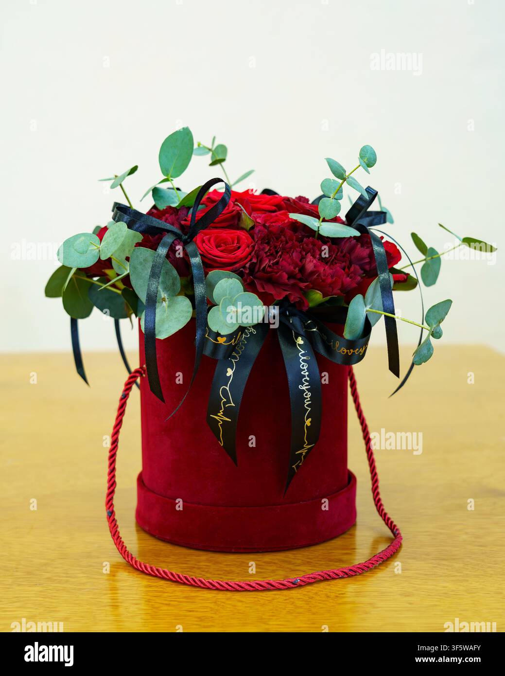 Bouquet de roses rouges avec rubans et verdure dans une boîte ronde sur une table Banque D'Images