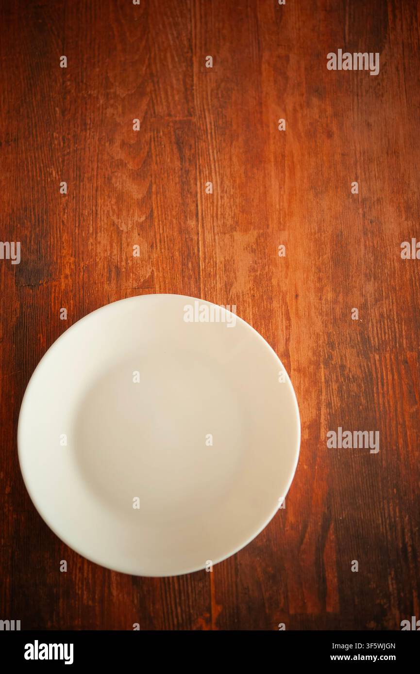 Assiette en céramique blanche vide sur une table en bois rustique, photographiée de dessus décentrée, avec un espace de copie généreux Banque D'Images