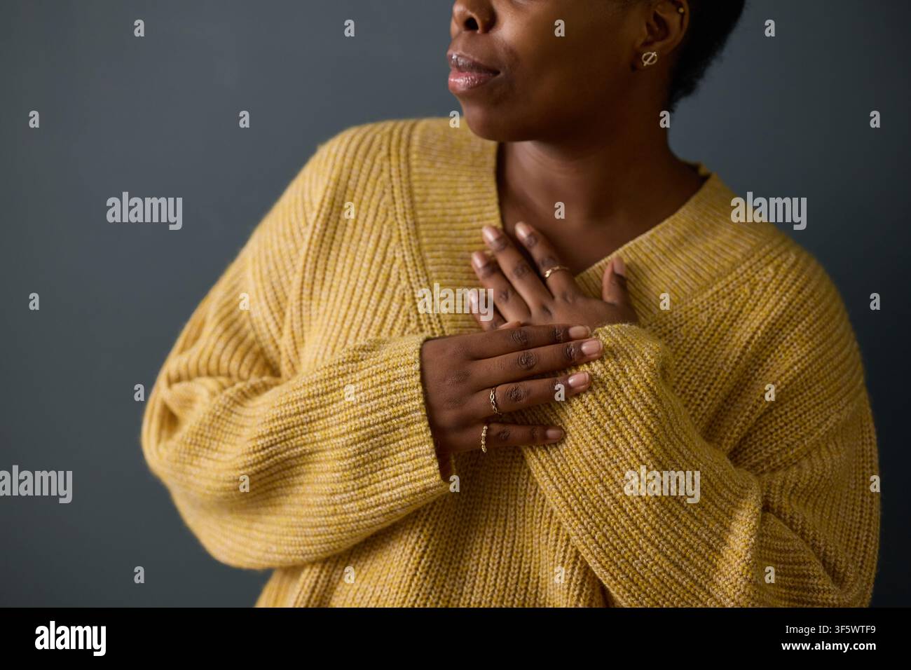 Jeune femme afro-américaine tenant les mains sur le cœur, exprimant la gratitude et les soins personnels. L'image représente le bien-être mental, la pleine conscience et le marketing de la santé émotionnelle Banque D'Images