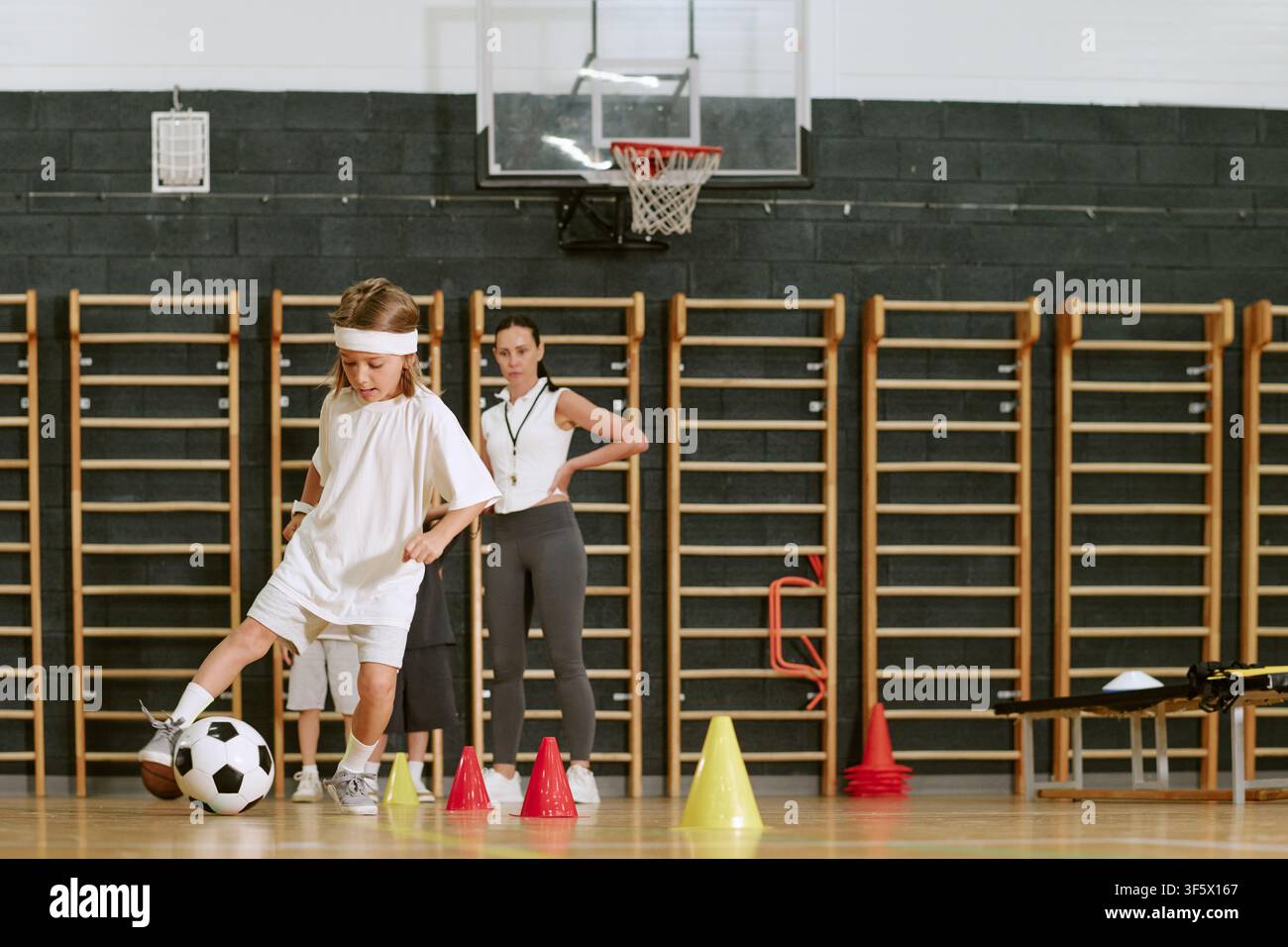 Entraîneuse féminine observant des enfants s'entraînant au football dans le gymnase scolaire Banque D'Images