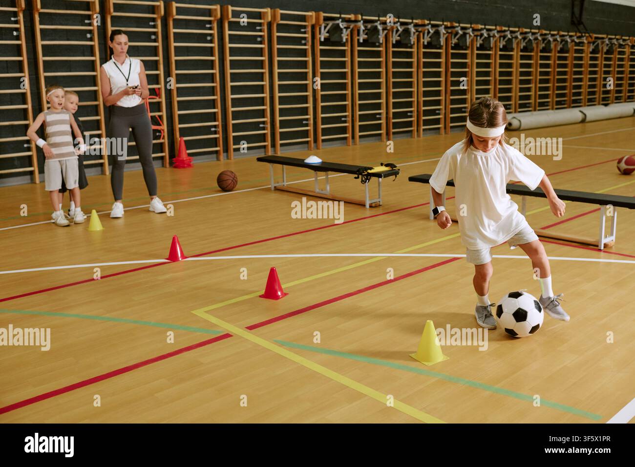 Entraîneuse surveillant des enfants s'entraînant avec un ballon de football dans la salle de gym Banque D'Images