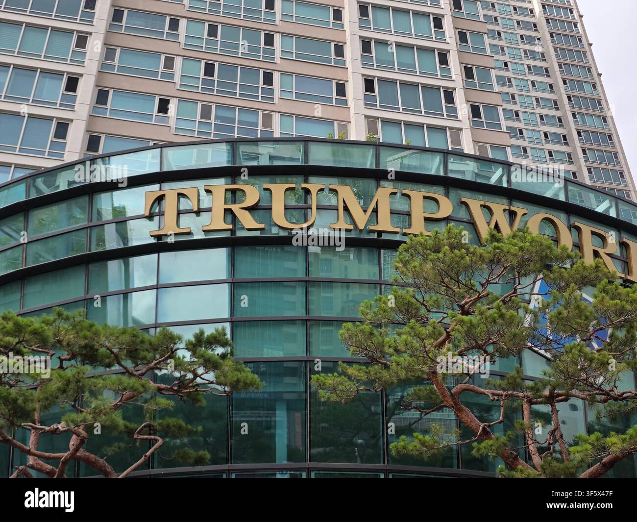 Prise de vue en contre-plongée de la façade extérieure du bâtiment Trump World avec de grandes lettres dorées, une structure en verre incurvée et des pins verts dans le Banque D'Images