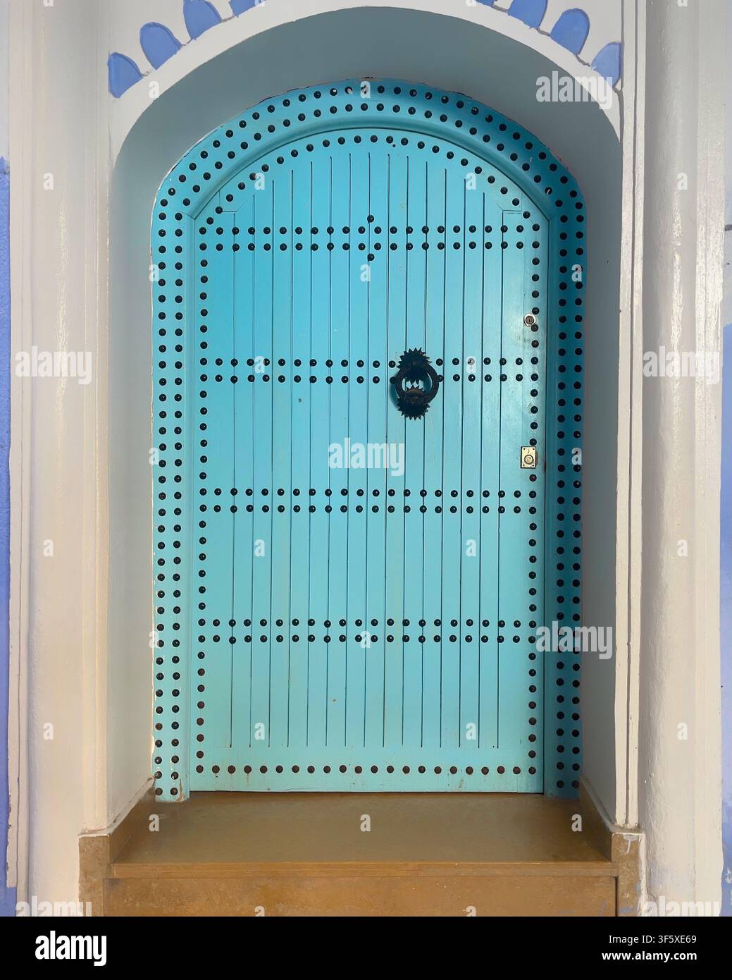 Porte voûtée turquoise élégante avec clous décoratifs et heurtoir noir, typique de l'architecture marocaine à Chefchaouen dans la Cité Bleue. Banque D'Images