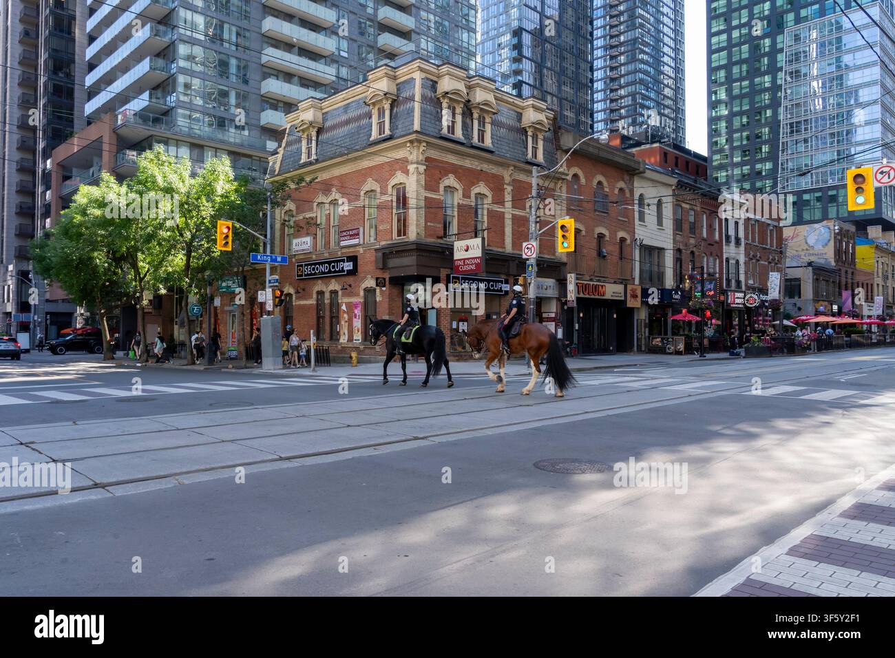 Deux agents de police à cheval traversent l'intersection de King Street West et John Street à Toronto Banque D'Images