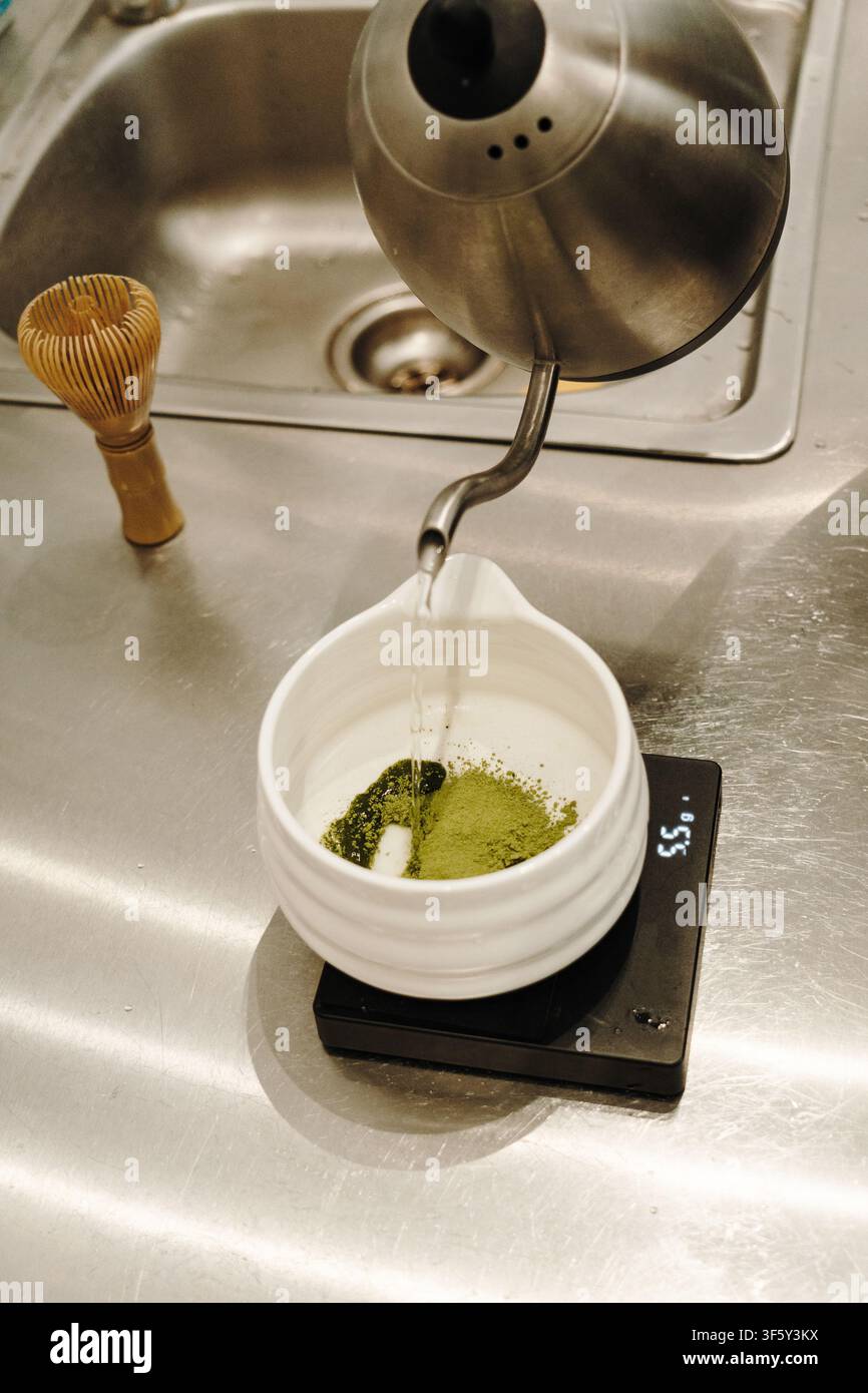 De l'eau chaude est versée sur de la poudre de matcha tamisée dans un bol en céramique posé sur une balance numérique. Préparation traditionnelle du thé japonais en cours. Banque D'Images