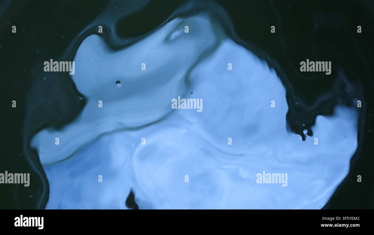 Une image abstraite d'une surface liquide sombre et brillante avec une réflexion floue bleu doux du ciel ou des nuages. Des formes lisses et déformées créent un miroir Banque D'Images