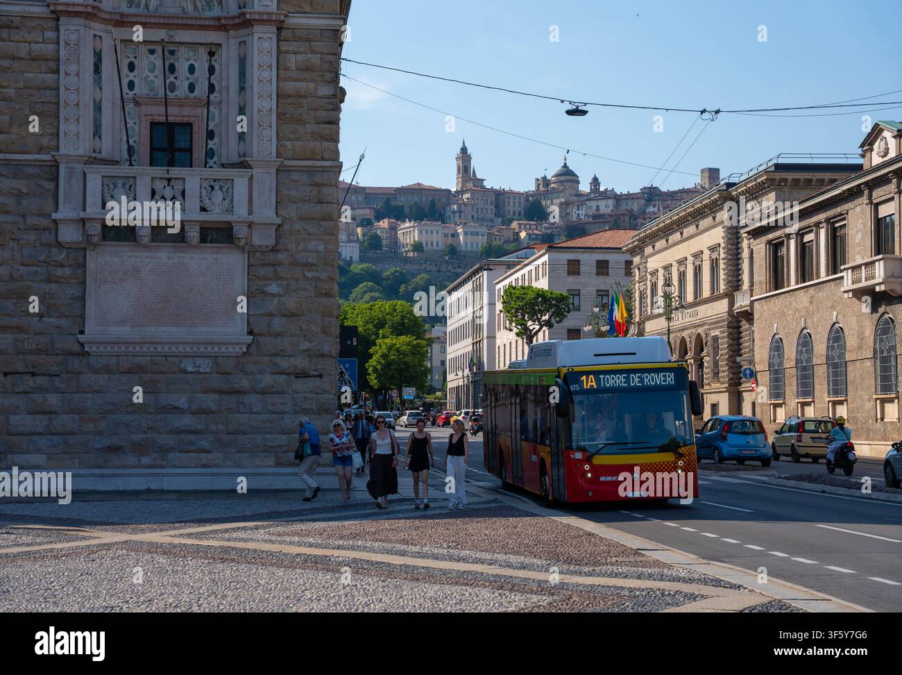 Bergamo, Italie – 16 juin 2026 : Bus public circulant le long d'une route urbaine dans la ville basse de Bergame avec un bâtiment historique en pierre, des piétons et vue sur la Citta Alta Banque D'Images