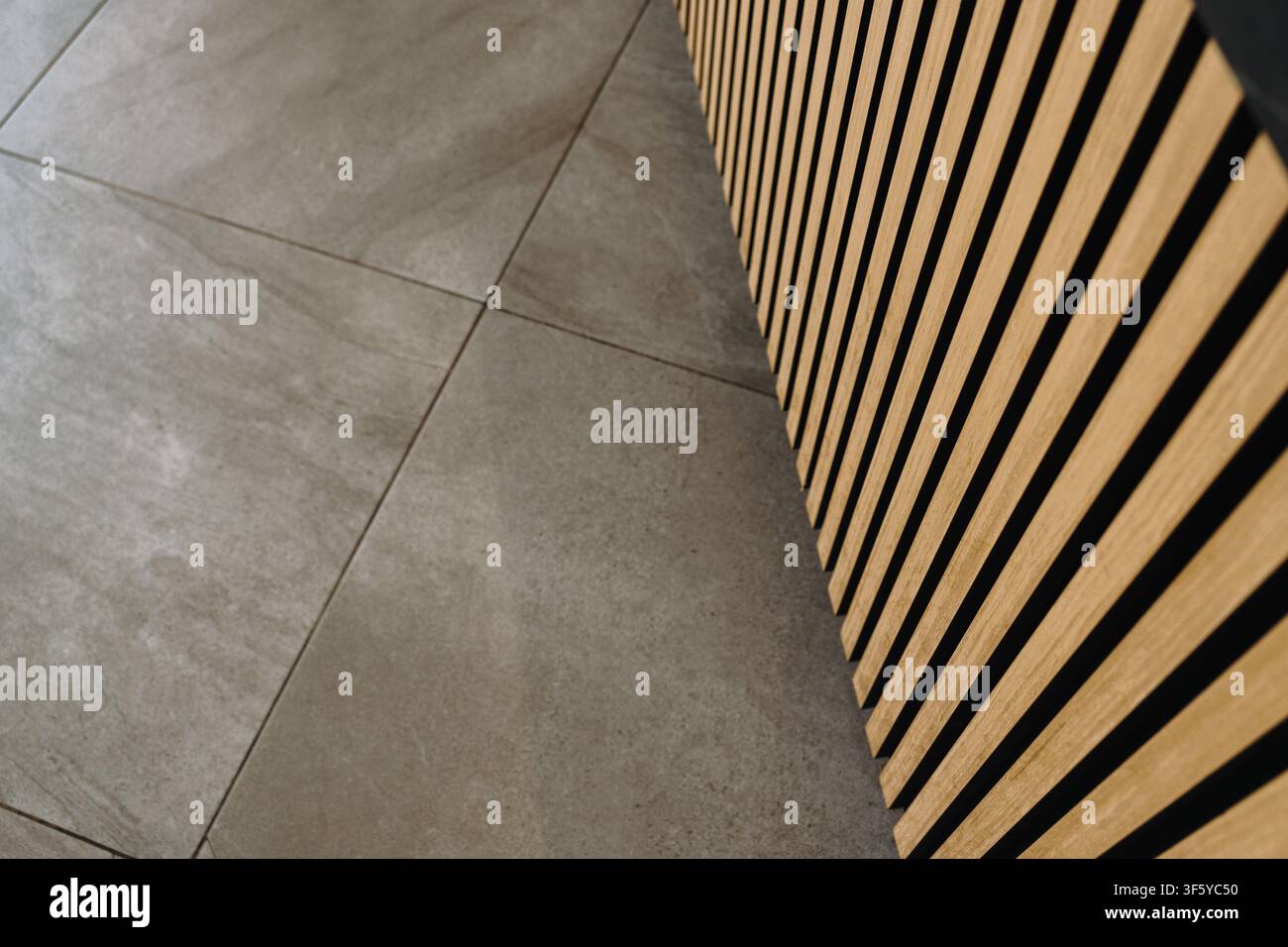 Détail intérieur minimaliste mettant en avant des panneaux muraux en lattes de bois et un sol carrelé gris. Fond architectural contemporain avec des lignes géométriques épurées. Banque D'Images