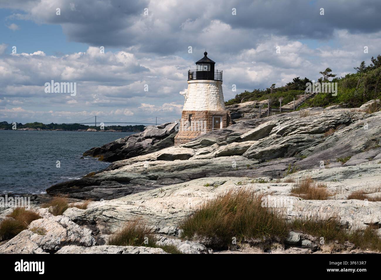 Phare de Castle Hill, Newport, Rhode Island, avec un avant-plan rocheux, un ciel nuageux, le pont Claiborne Pell en arrière-plan Banque D'Images