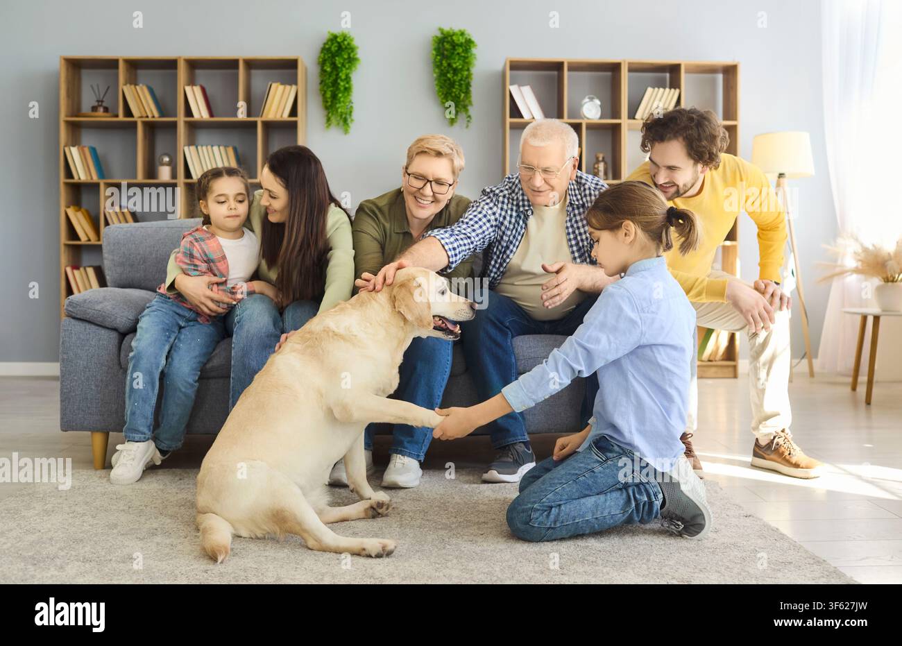 Famille élargie joyeuse regardant un enfant entraîner un labrador à la maison, poignée de patte amicale Banque D'Images