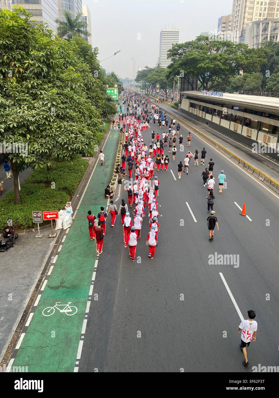 Des piétons et un groupe en marche en uniforme défilent le long d'une rue sans voitures à Jakarta, en Indonésie, avec la ligne d'horizon de la ville en arrière-plan - Image de stock capturée avec un smartphone