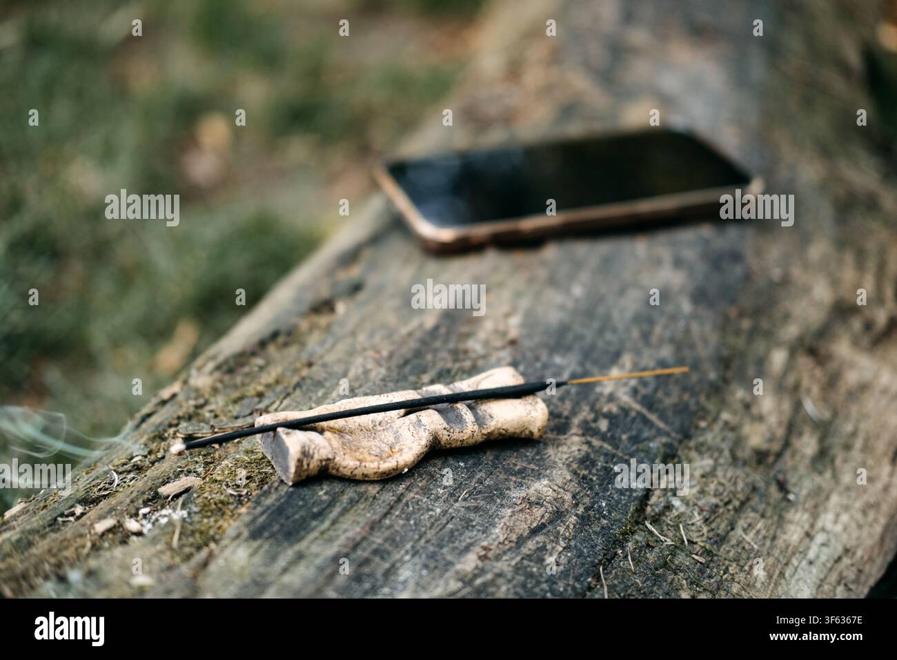 Smartphone posé écran vers le bas sur une bûche en bois patiné à côté d'un bâton d'encens. Téléphone mis de côté, détox numérique dans la nature, se déconnecter de l'écran en plein air Banque D'Images