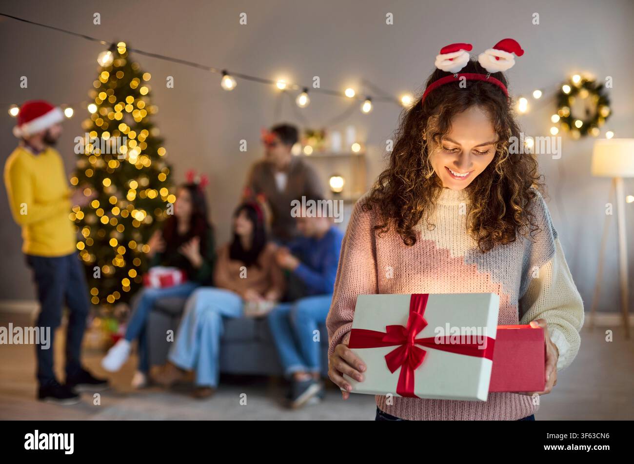 Femme heureuse ouvrant une boîte cadeau de Noël lors d'une fête chaleureuse à la maison avec amis et famille Banque D'Images