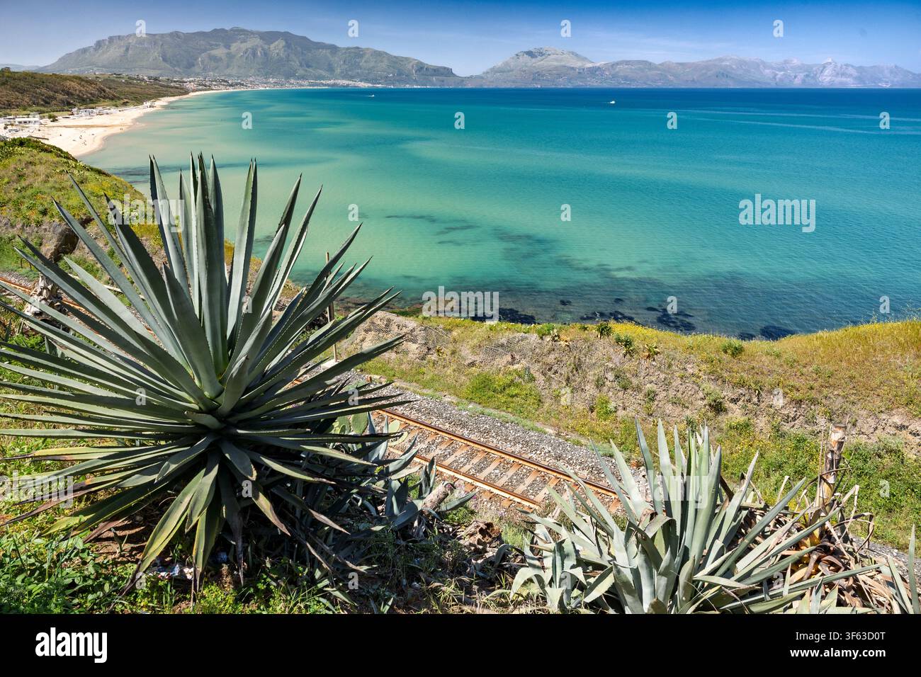 Vue panoramique de la côte sicilienne mettant en scène des plants d'agave et des voies ferrées surplombant une baie turquoise et une plage, Balestrate, Sicile, Italie. Banque D'Images