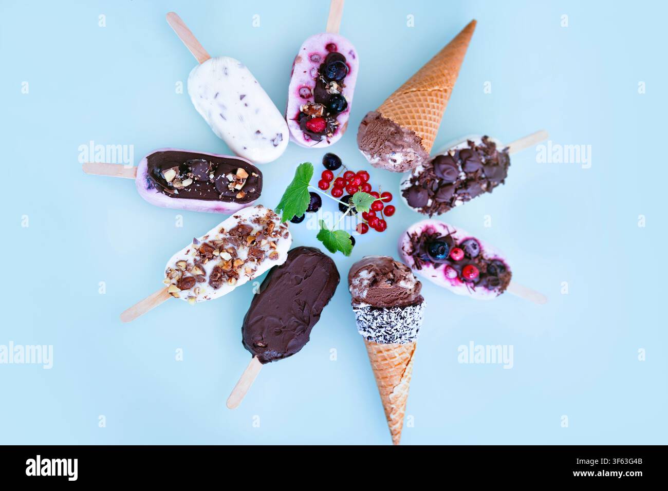 Ronde colorée de bâtonnets glacés maison au yaourt et au lait. Vanille et chocolat décorés de noix et de baies surgelées sur un fond bleu vif. Parfait pour une fête d'anniversaire d'enfants en été. Banque D'Images