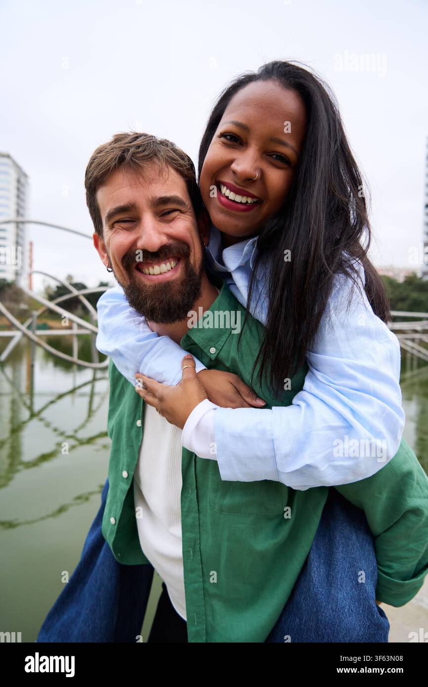 Heureux couple multiracial piggyback et souriant à l'extérieur. Banque D'Images