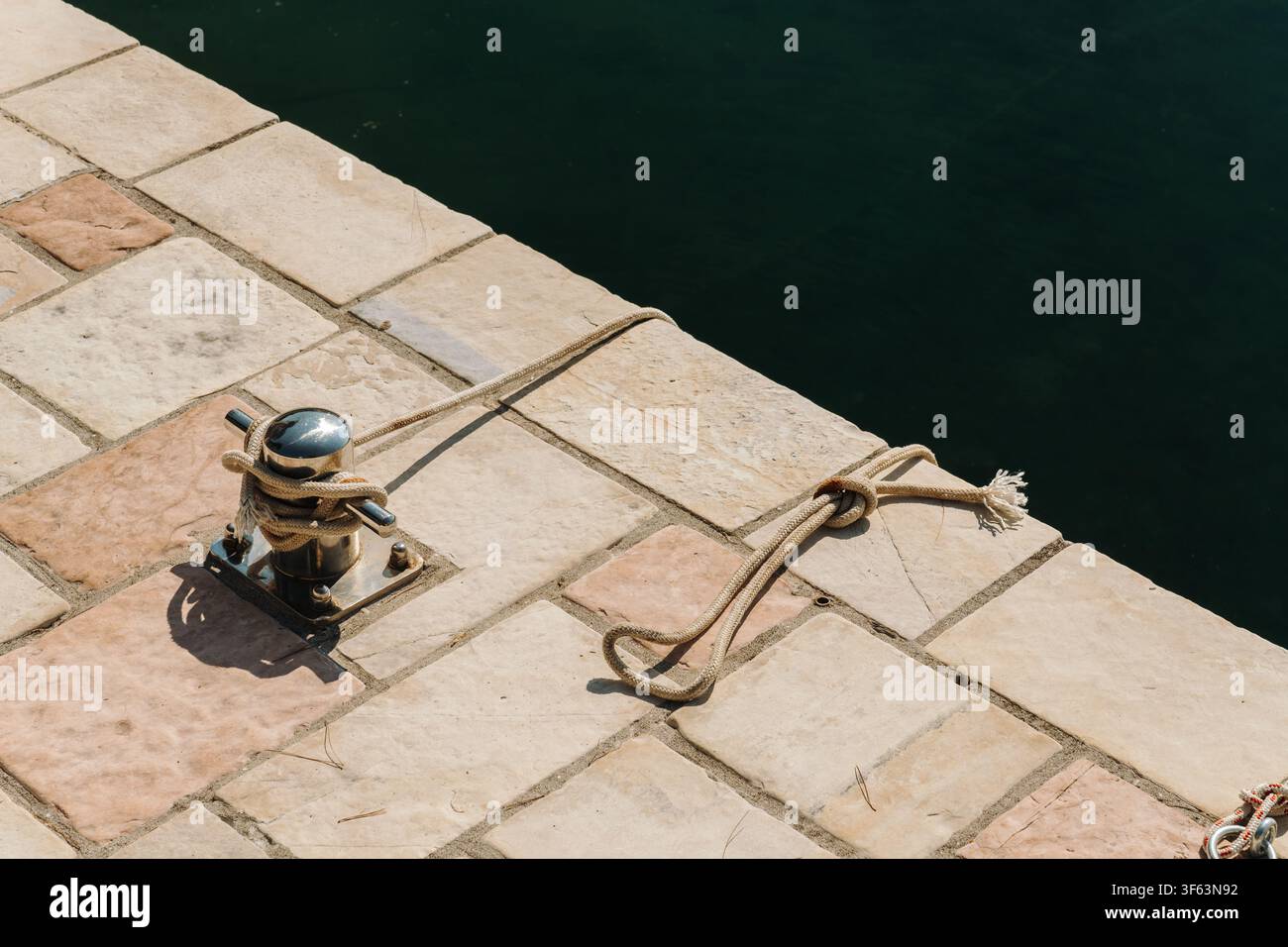 Corde marine fixée à une bitte en acier inoxydable à côté d'une eau calme. Détail nautique montrant un équipement d'amarrage de bateau au bord de l'eau Banque D'Images