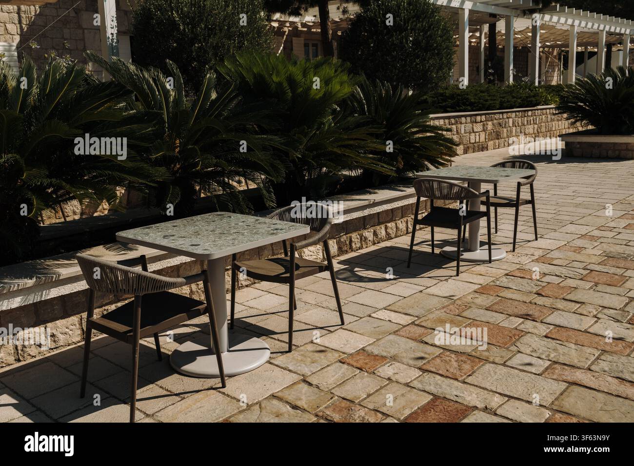 Terrasse extérieure moderne de café avec des tables et des chaises vides entourées d'une végétation luxuriante. Cadre d'hospitalité paisible sous la lumière chaude du soleil d'été. Banque D'Images