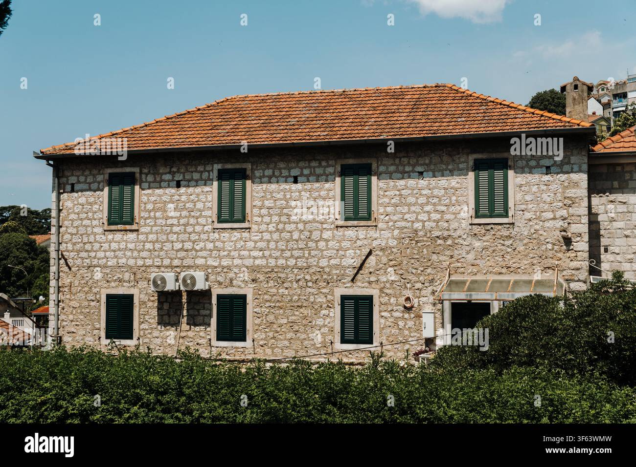 Maison en pierre traditionnelle avec volets verts et toit en tuiles sous un ciel bleu éclatant. L'architecture méditerranéenne classique reflète l'intemporalité Banque D'Images