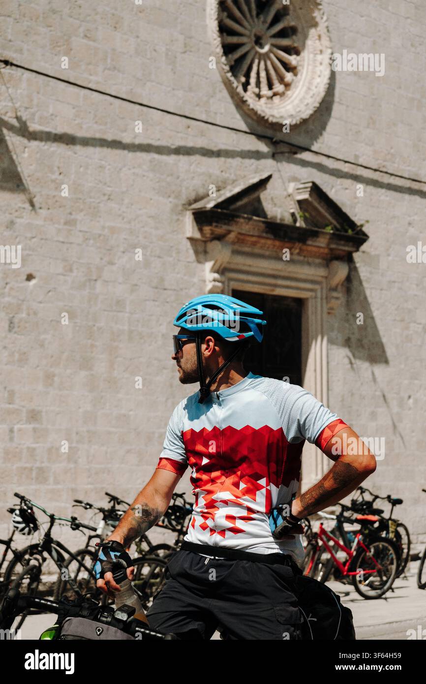 Vue rapprochée d'un cycliste à côté d'une église historique à Prcanj sur la baie de Kotor. Tournée à vélo estivale le long de la côte méditerranéenne du Monténégro. Banque D'Images