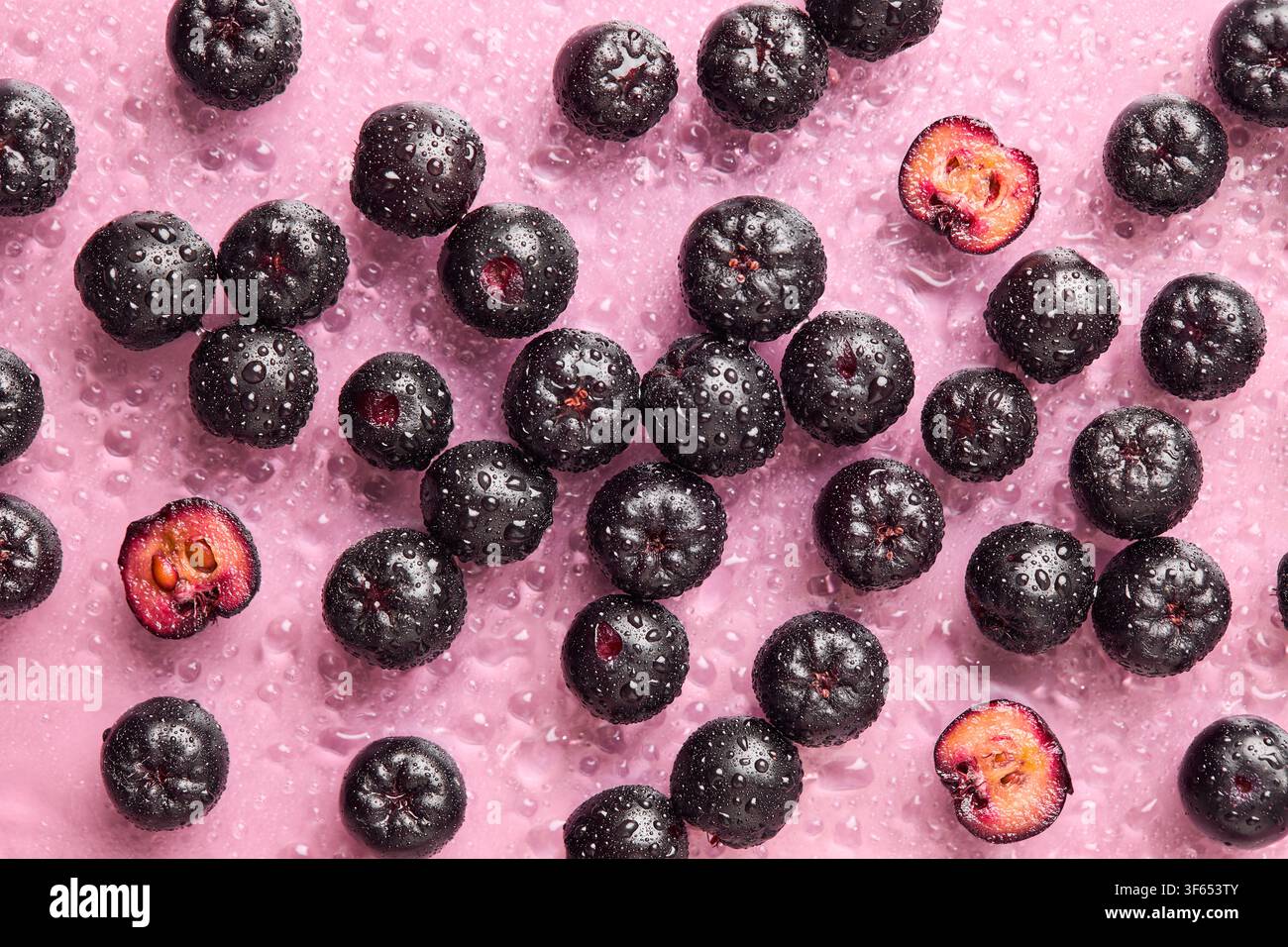 Baies d'aronia fraîches avec des gouttelettes d'eau sur un fond rose. Concept de fruits d'été sains. Banque D'Images