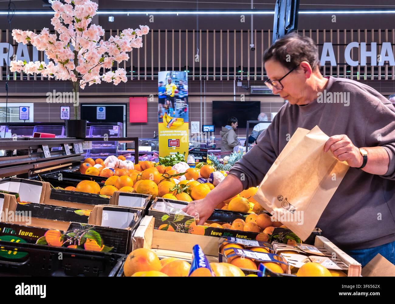Dijon Bourgogne France 12 mai 2026. Femme adulte choisissant des agrumes frais et les plaçant soigneusement dans un sac en papier écologique dans un su local Banque D'Images