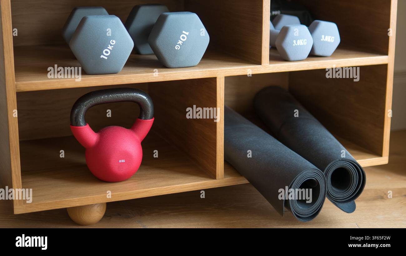 Équipement de gym domestique soigneusement organisé avec des haltères, un kettlebell rouge et des tapis de yoga roulés sur des étagères en chêne — Fitness à domicile, bien-être et rangement intérieur Banque D'Images