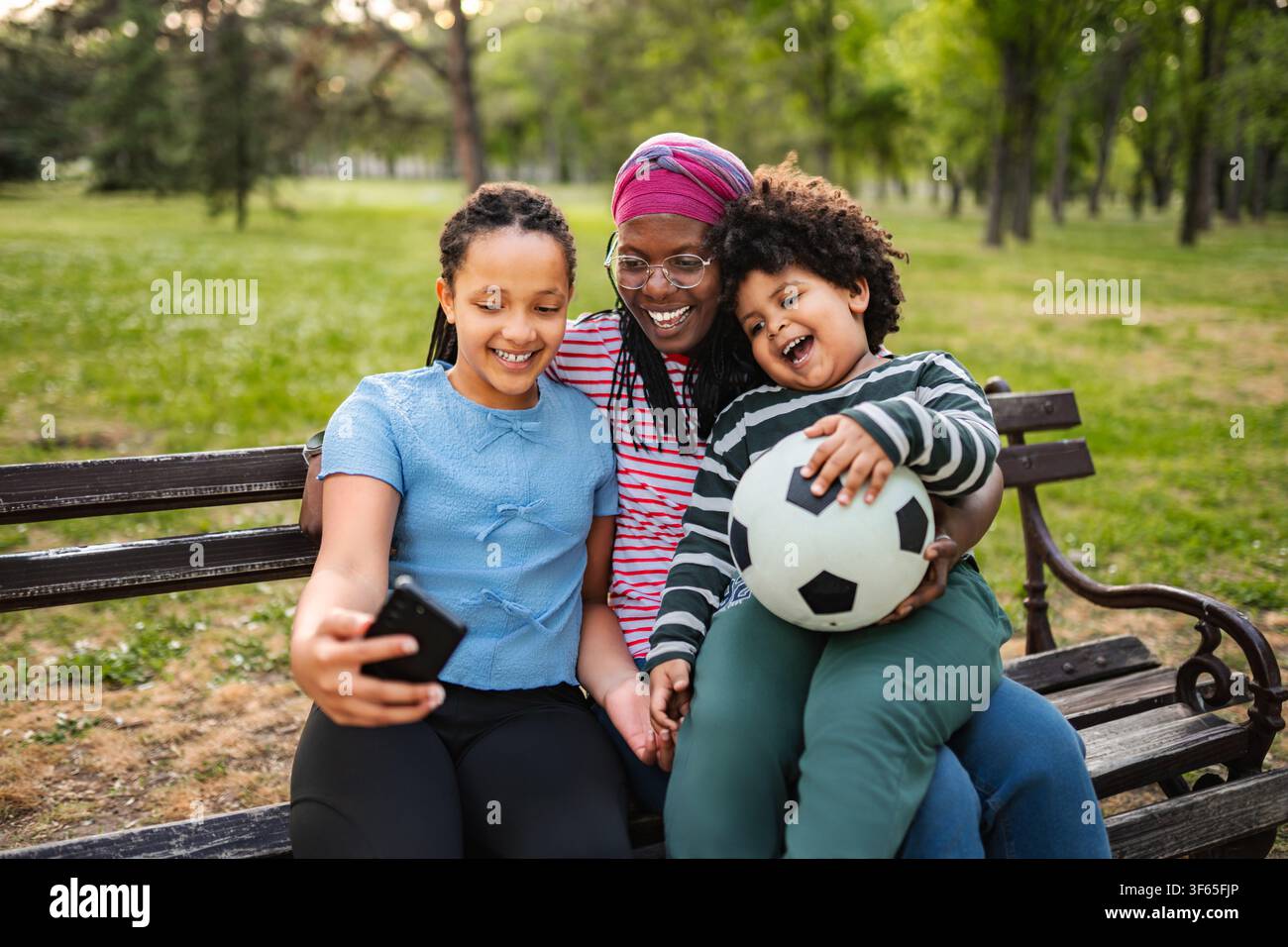 Mère et enfants prenant un selfie en train de créer des liens au parc Banque D'Images