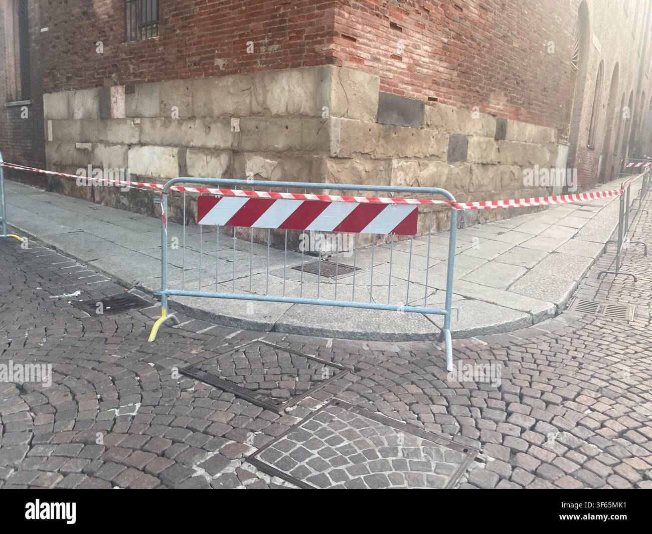 Cremone, Italie, 15 juillet 2026 Barrière temporaire limitant l'accès sur une rue pavée mouillée, montrant les conséquences d'un orage après une vague de chaleur Banque D'Images