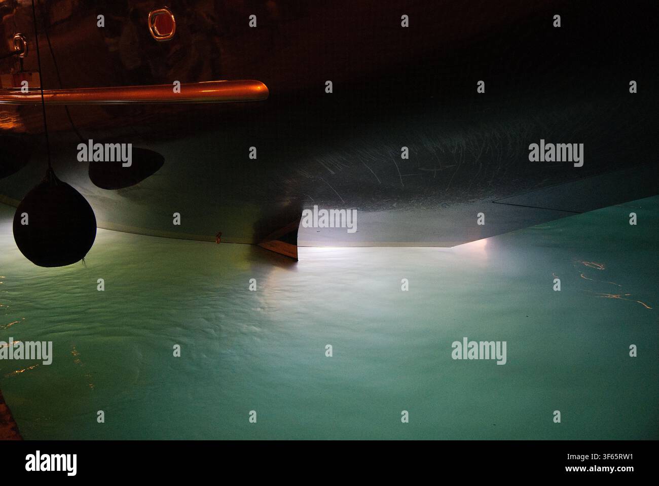 Des lumières sous-marines brillant sous la coque d'un yacht de luxe amarré la nuit, créant un reflet turquoise vif dans l'eau sombre du port. Banque D'Images