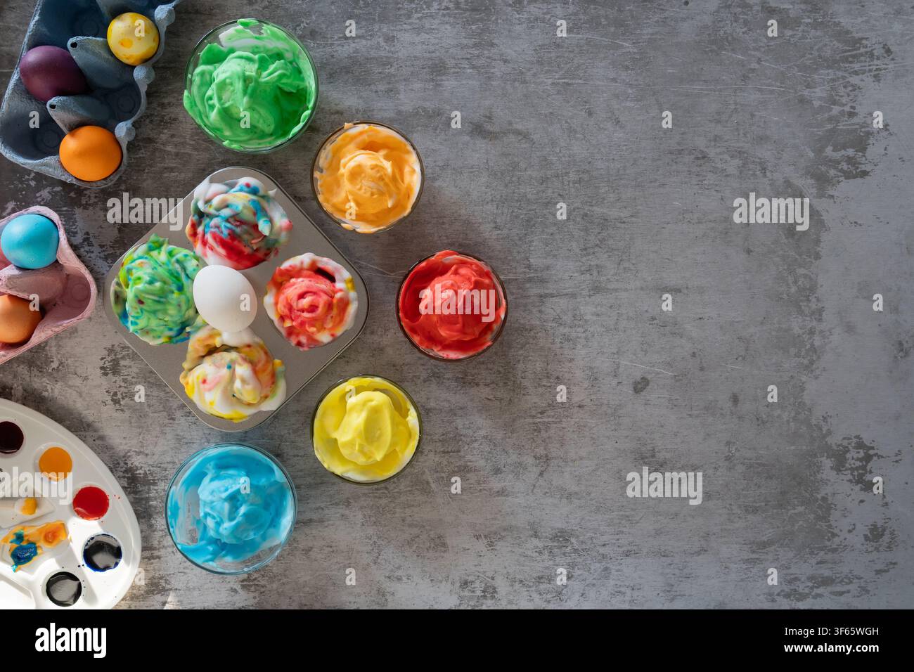 Des œufs de Pâques fraîchement teints reposant dans de la mousse à raser sur une table grise pendant le processus de marbre pour des décorations de Pâques colorées Banque D'Images