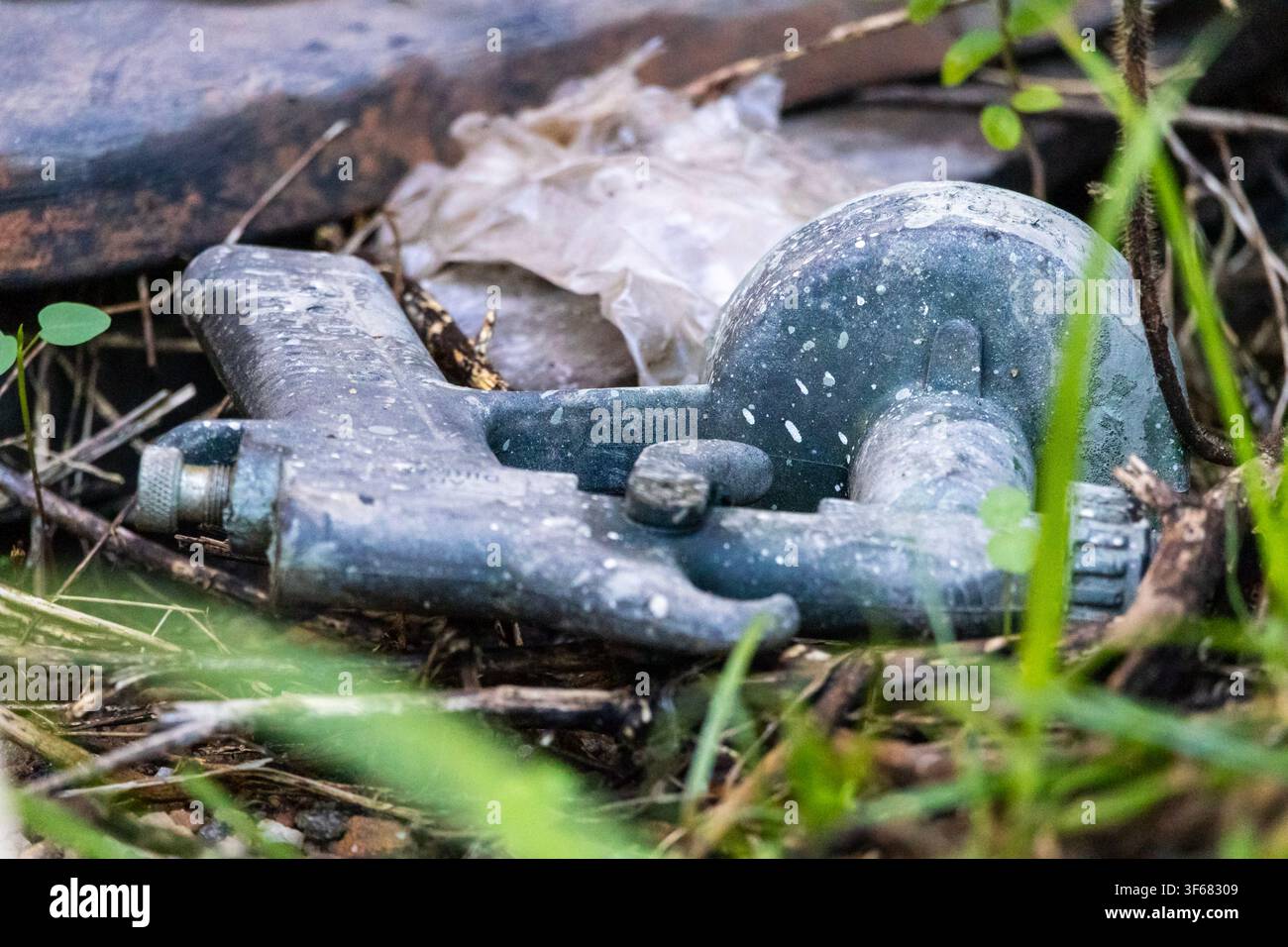 Grossissement d'un pistolet de pulvérisation de peinture abandonné au sol avec des gouttelettes de peinture partout et un premier plan vert doux Banque D'Images