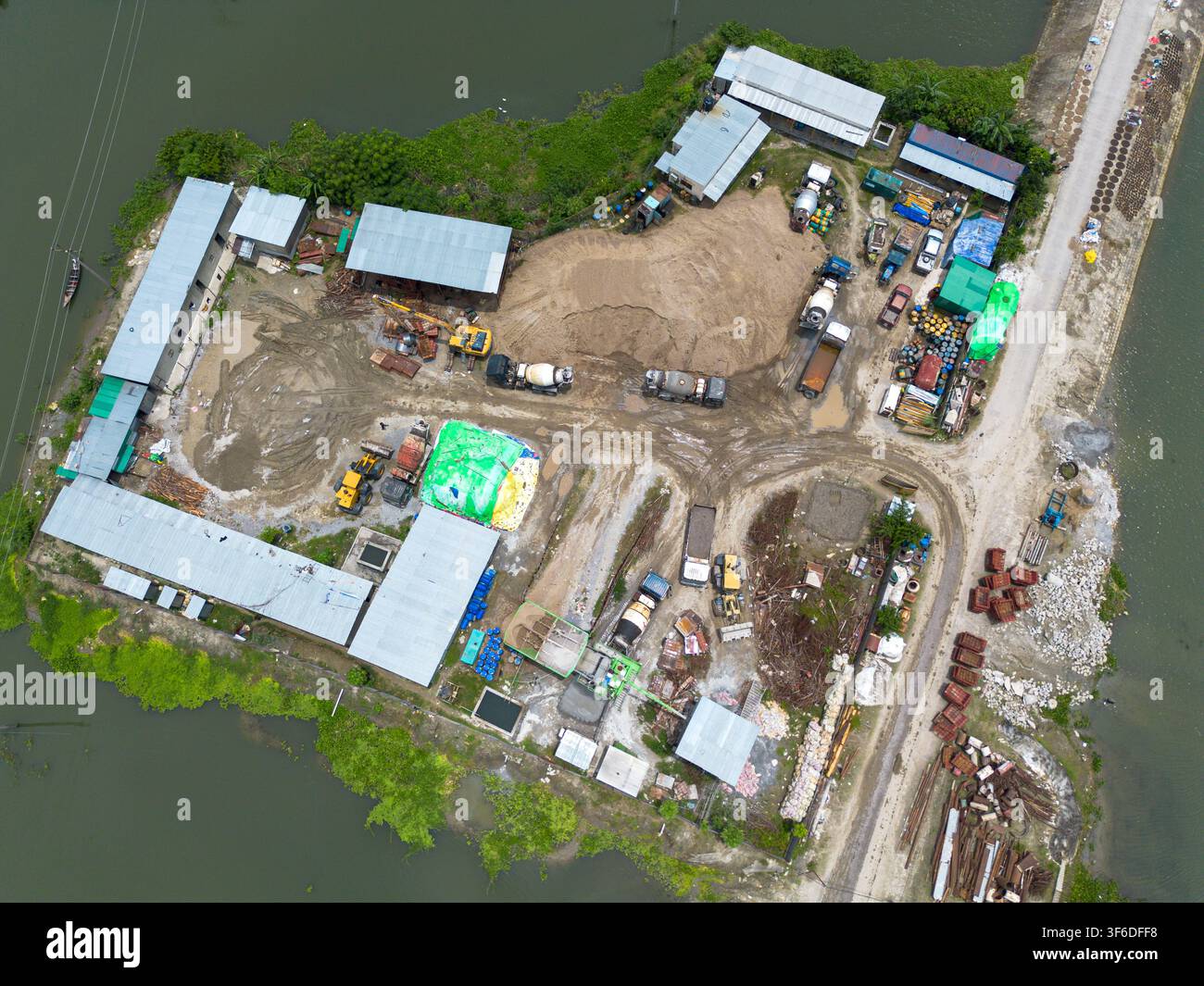Vue aérienne d'un chantier de construction mettant en scène des machines lourdes, des bétonneuses et des tas de sable sur une péninsule entourée d'eau à Kishoreganj, Dh Banque D'Images