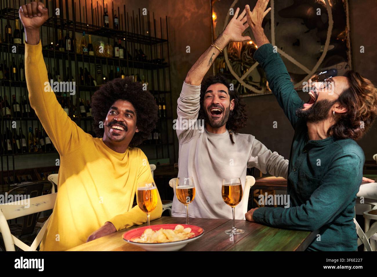 Groupe multiracial d'amis de sexe masculin regardant un match de football au bar. Célébrez un score, avec les poings vers le haut Banque D'Images