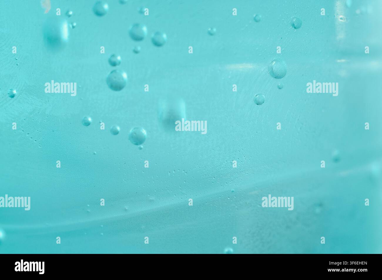 Macro de l'eau gazeuse montrant de petites bulles ascendantes flottant dans un récipient transparent turquoise avec des gouttes de condensation. Banque D'Images