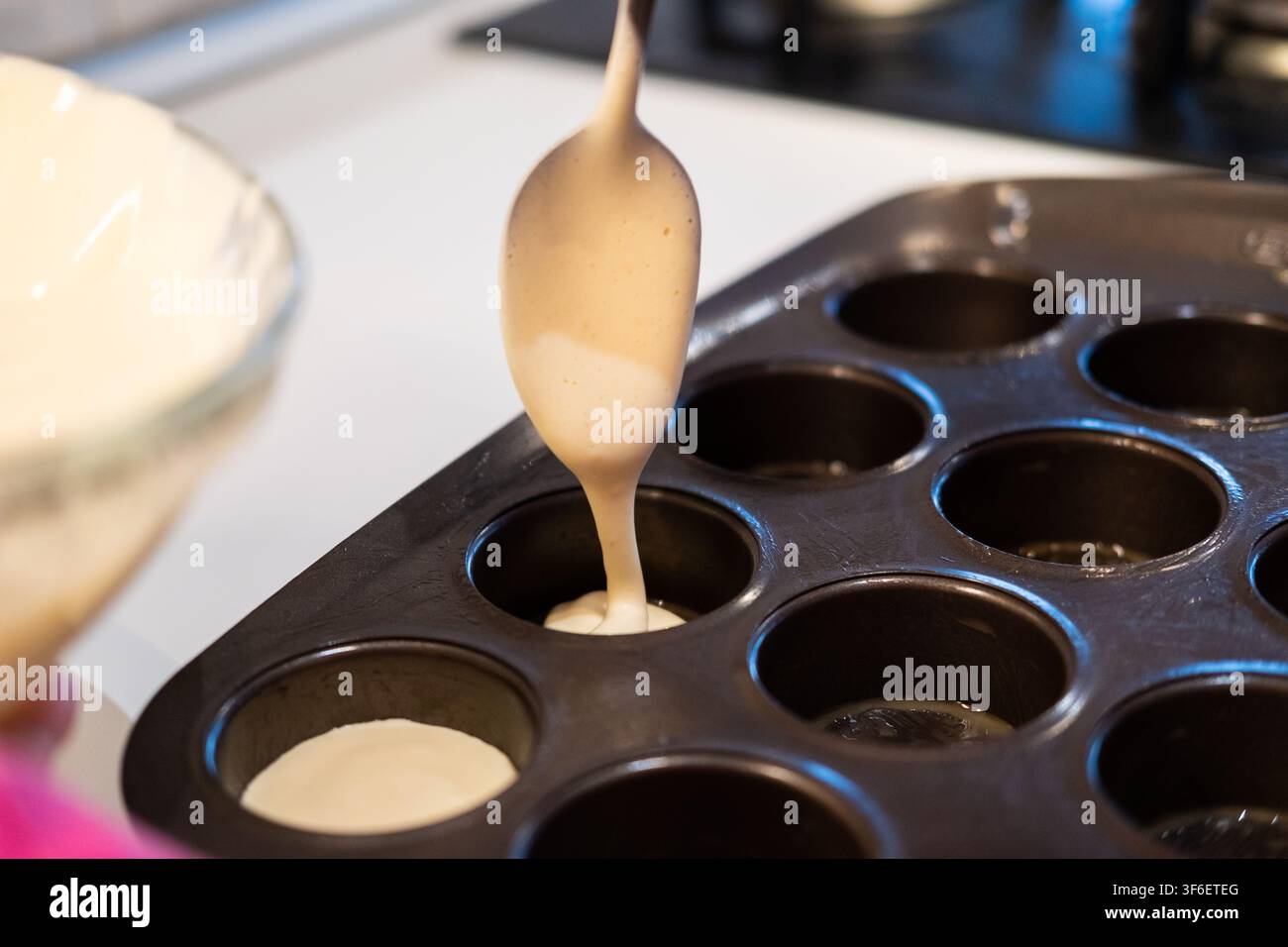 Person versant une pâte crémeuse dans un moule à muffins, préparant des desserts faits maison Banque D'Images