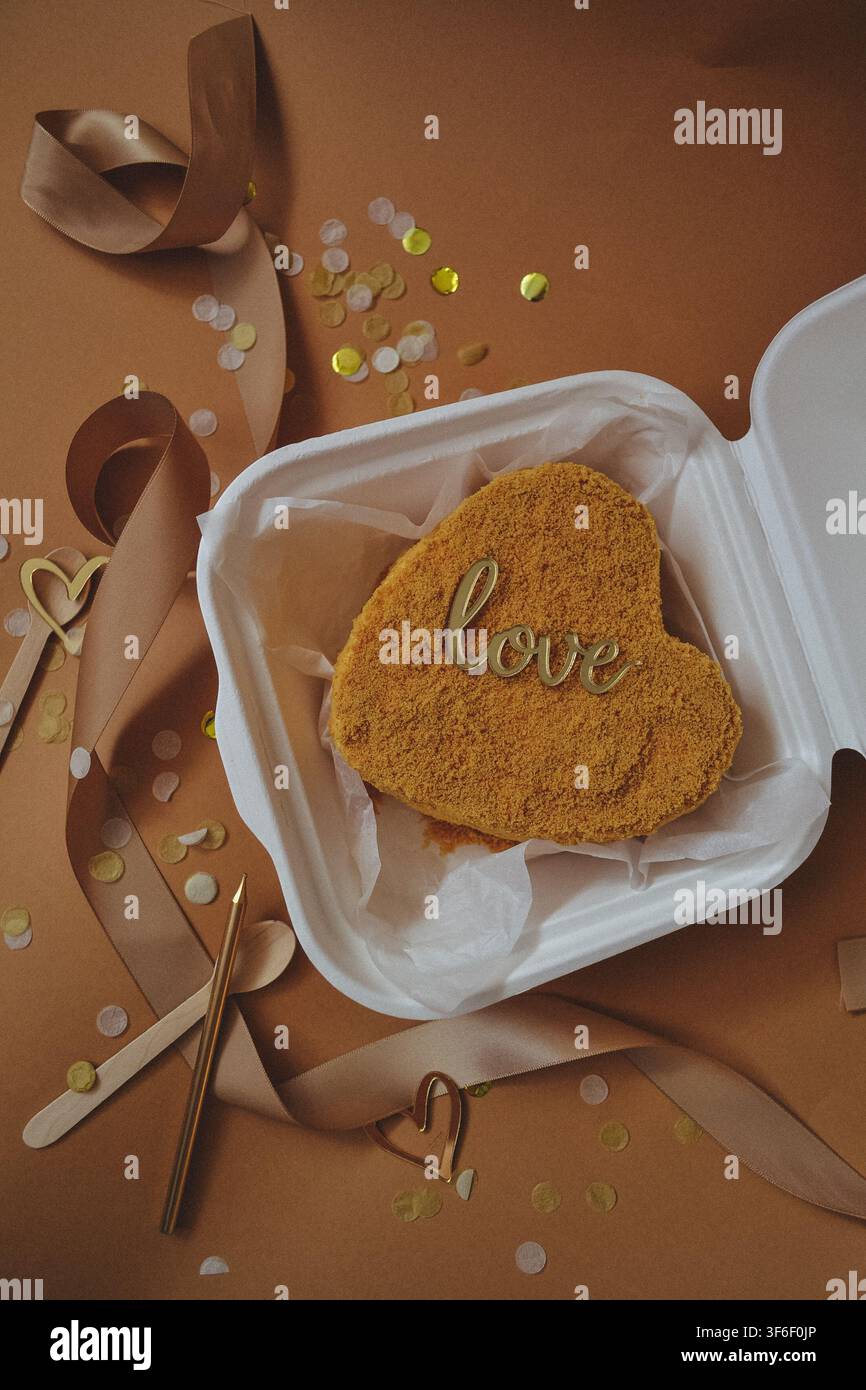 Gâteau bento en forme de cœur avec un signe d'amour dans un contenant blanc à emporter sur fond beige, concept de la Saint-Valentin Banque D'Images