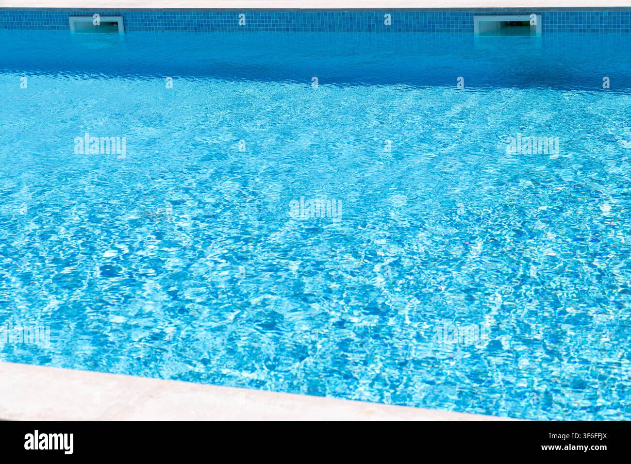 La surface d'une piscine bleu vif reflète la lumière du soleil, créant des motifs chatoyants à la surface de l'eau Banque D'Images