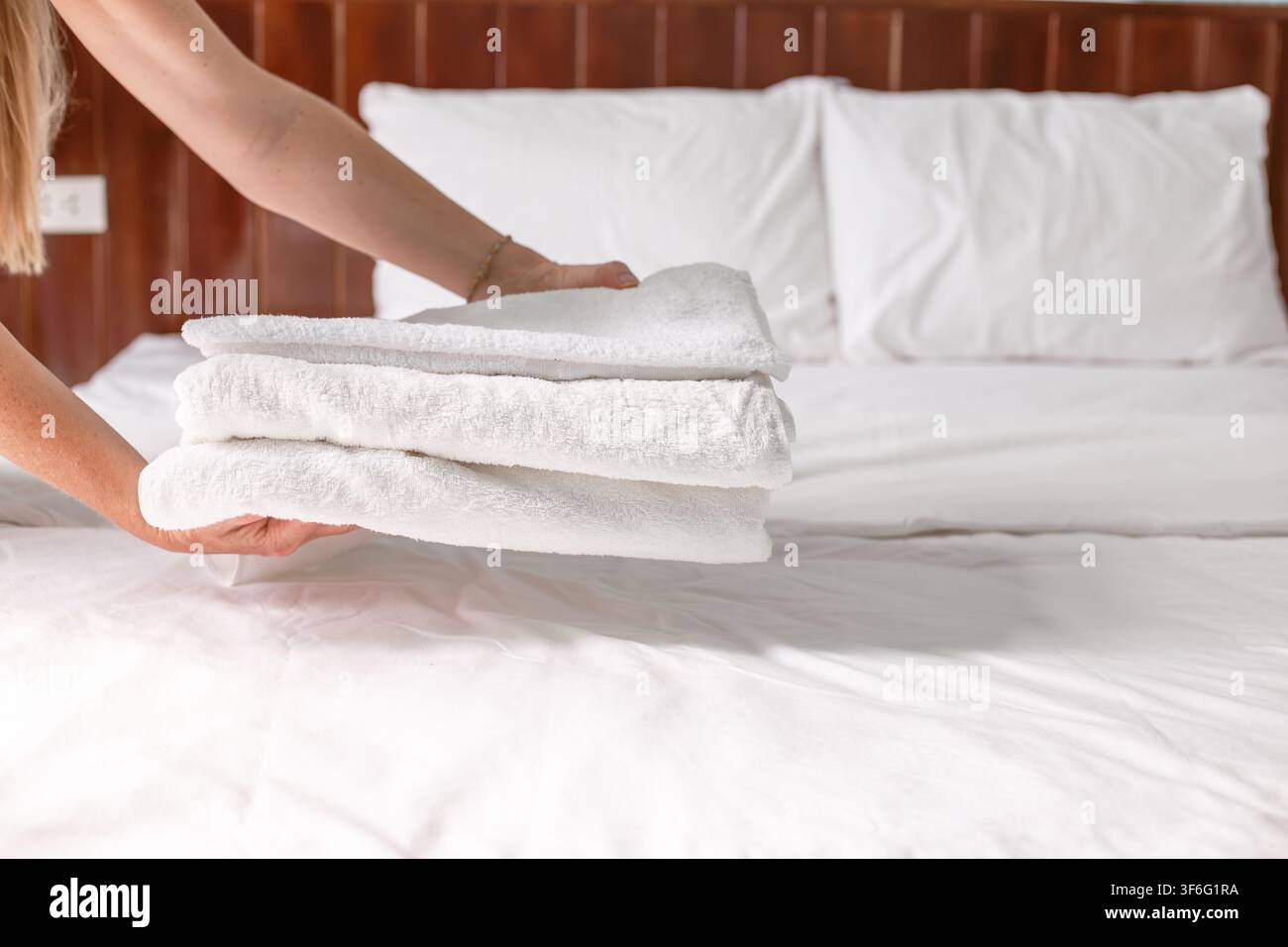 Chambre d’hôtel où une femme de ménage pose une pile de serviettes blanches fraîchement pliées sur un lit parfaitement fait. Service de chambre d’hôtellerie, intérieur d’hôtel propre. Banque D'Images