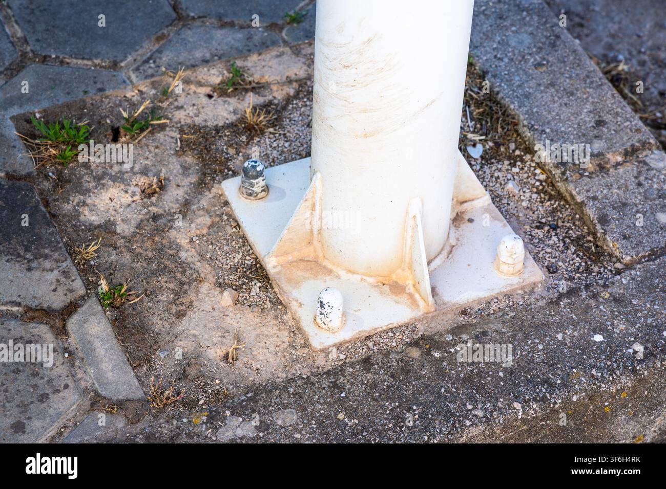 Une vue détaillée de la fondation d'un poteau cylindrique blanc, montrant sa plaque de base en métal fixée par des boulons dans une dalle de béton et le pavage environnant Banque D'Images