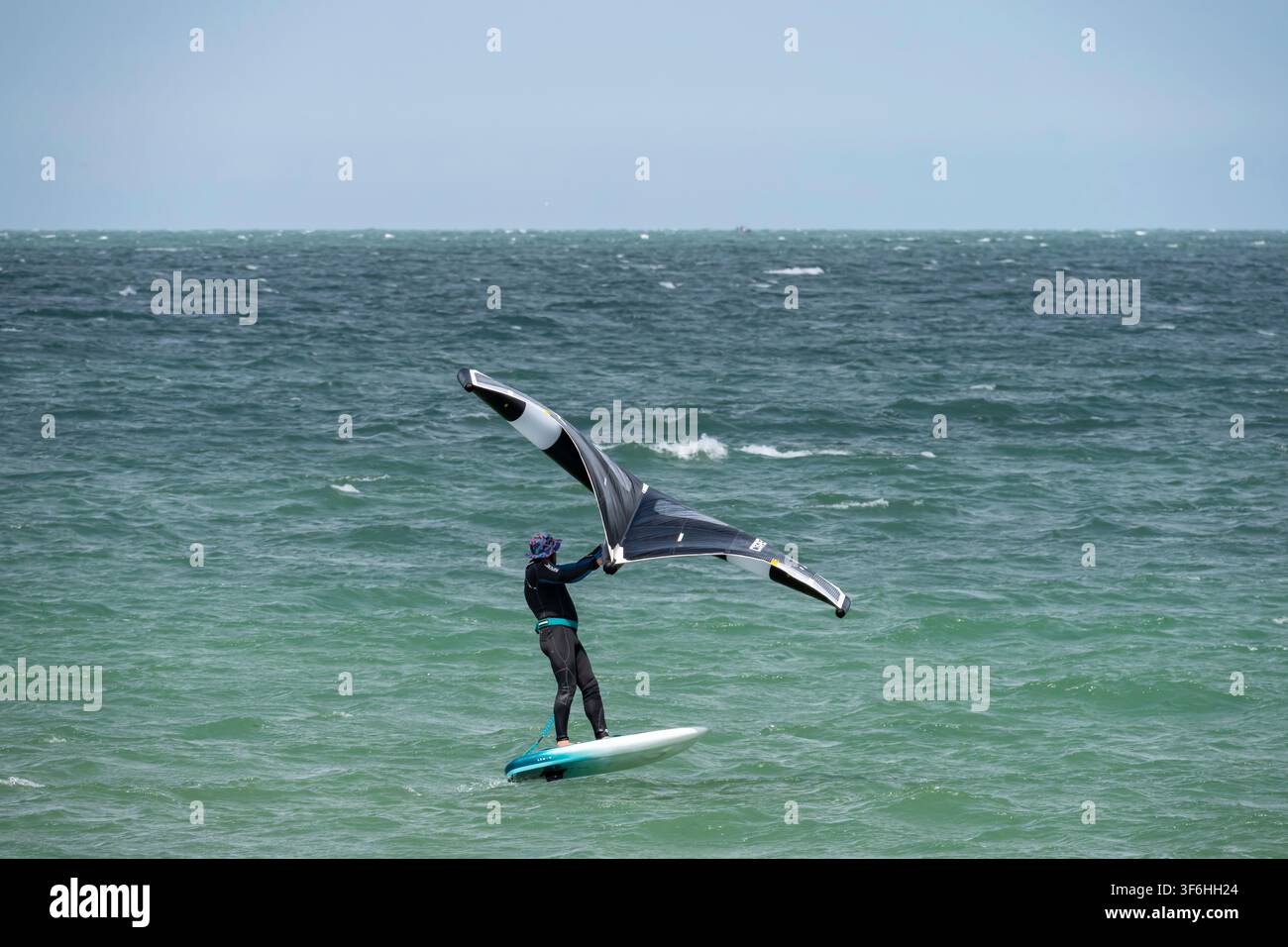 Langrune-Sur-Mer, France - 08 05 2026 : Un planchiste portant une combinaison de plongée surfe avec un wingsurf sur la mer Banque D'Images